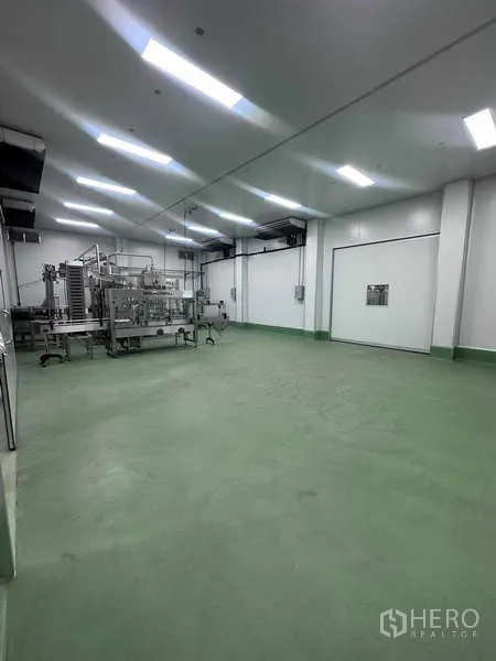 Factory for rent - Spacious cleanroom with green epoxy floor, overhead lights, and production machinery beside a white insulated door.