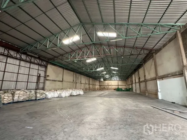 Warehouse for rent in Mueang Pathum Thani, Pathum Thani - Clear-span warehouse bay with insulated roof and palletized goods along the wall.