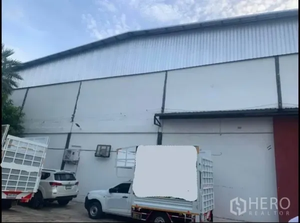 货栈 出租在Sai Noi, Nonthaburi - 仓库正立面，金属雨棚下的停车位与货运卡车