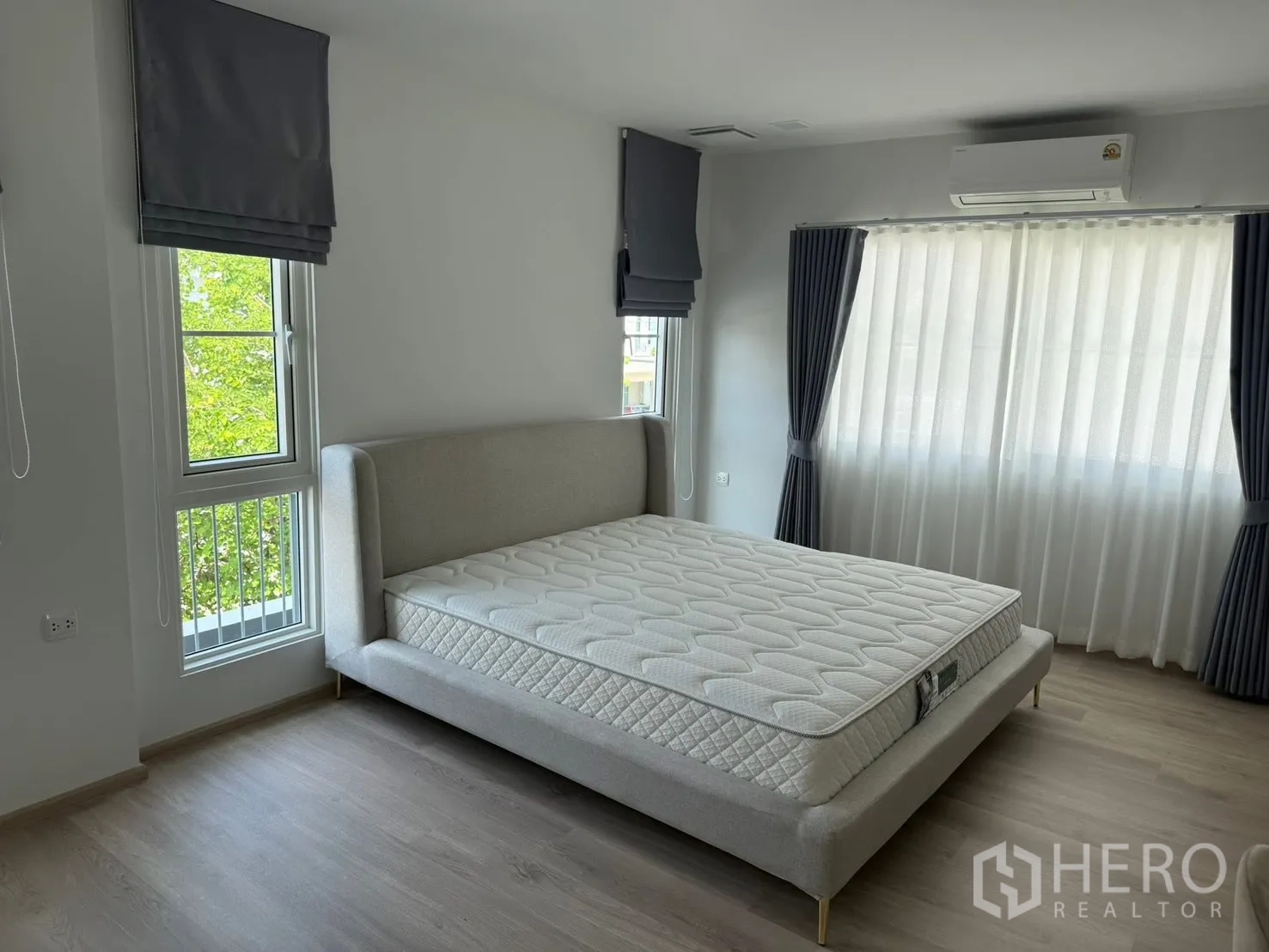 Detached House for rent in Bang Phli, Samut Prakan - Corner bedroom with upholstered bedframe, big windows, and air conditioner.