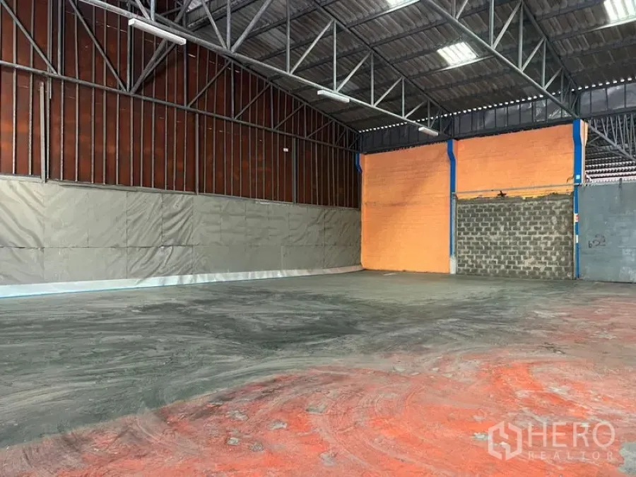 Warehouse for rent in Mueang Samut Prakan, Samut Prakan - Spacious warehouse interior with high steel trusses, orange partition wall and concrete floor.