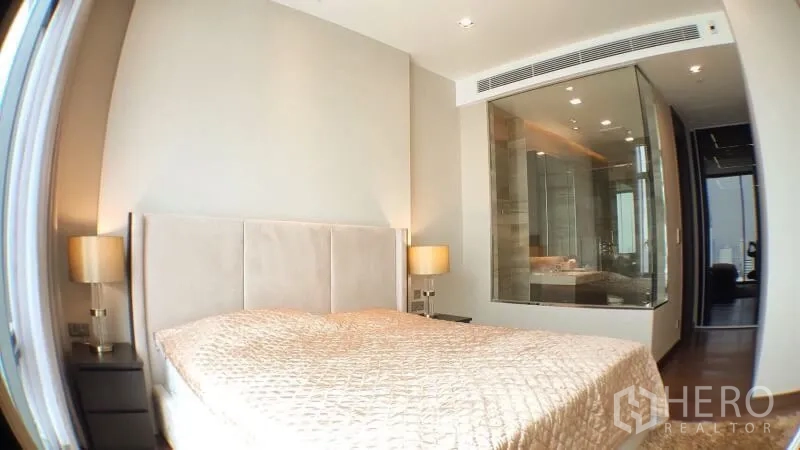 Condominium for rent in Khlong Toei, Bangkok - Bright master bedroom with padded headboard and glass-walled en-suite bathroom.