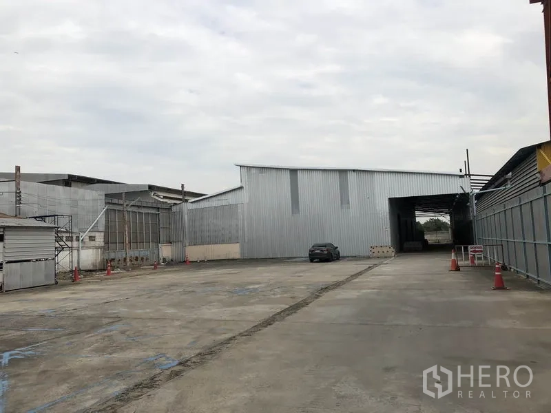 Warehouse for rent in Pak Kret, Nonthaburi - Exterior service yard and driveway beside metal buildings, offering ample truck turning space.