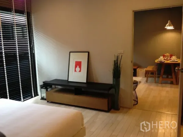 Condominium for rent in Watthana, Bangkok - Bedroom entry view showing media console, large window with blinds, and doorway to the dining area.