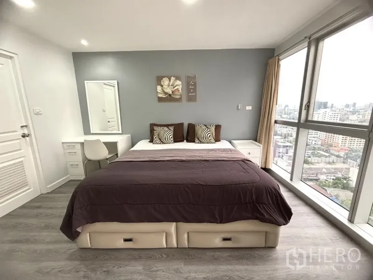 Condominium for sale in Khlong Toei, Bangkok - Bright master bedroom with king bed, grey accent wall, desk, and floor‑to‑ceiling city‑view windows.