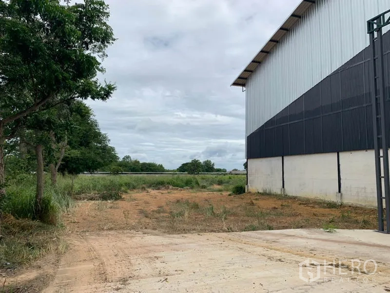 Factory for rent in Chon Buri - Side yard next to the factory with dirt access and greenery, suitable for loading or parking.