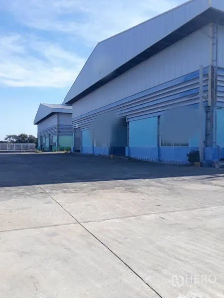Factory for rent in Samut Prakan - Front facade of blue and grey factory buildings with a large loading apron.