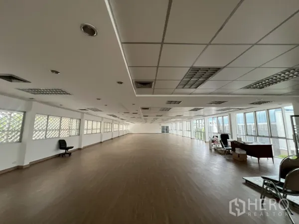 Office Space for rent in Watthana, Bangkok - Long rectangular office space with full-height windows and fluorescent ceiling lights.