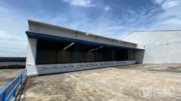 Factory for rent in Nonthaburi - Wide concrete forecourt with ramped access in front of a covered warehouse building.