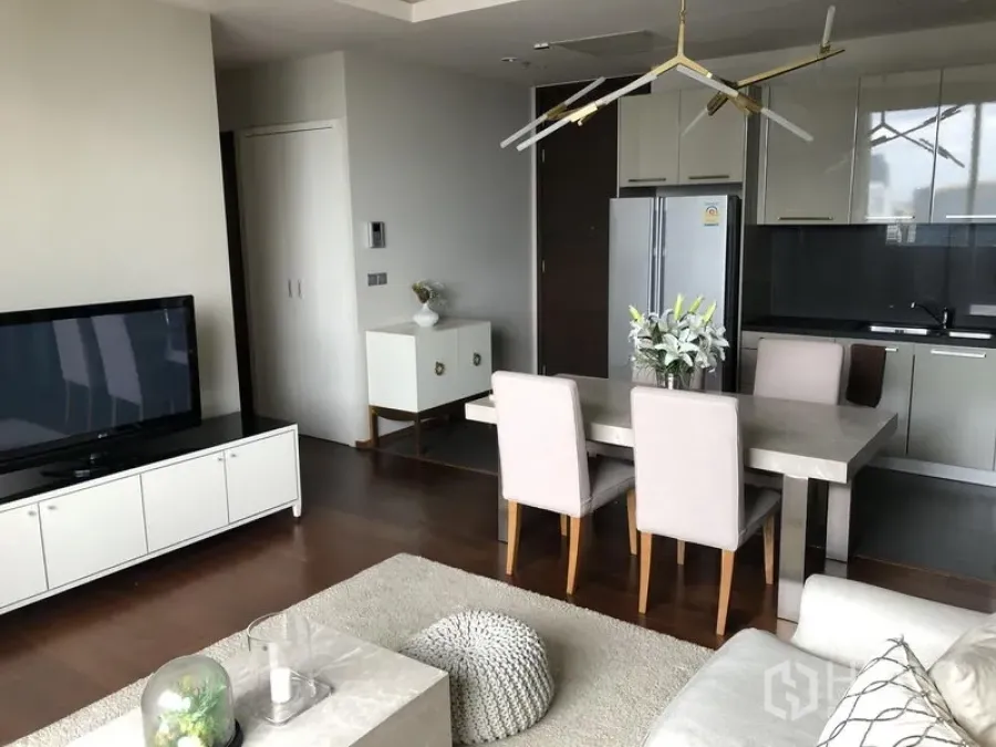 Condominium for rent in Watthana, Bangkok - Open-plan living and dining area with modern kitchenette, stone table, and dark wood flooring.
