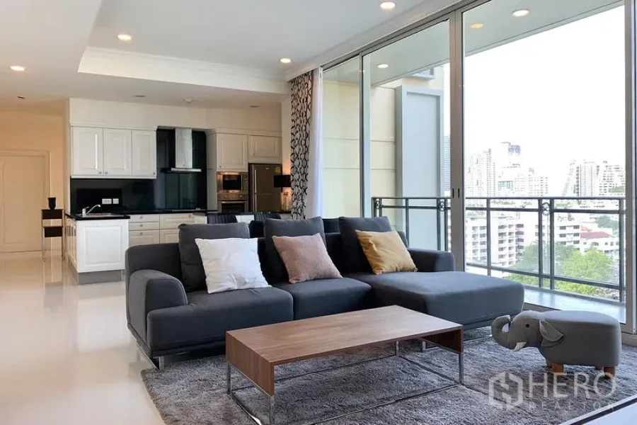 Condominium for rent in Watthana, Bangkok - Spacious lounge with L-shaped sofa, sliding glass doors to the balcony and skyline views.
