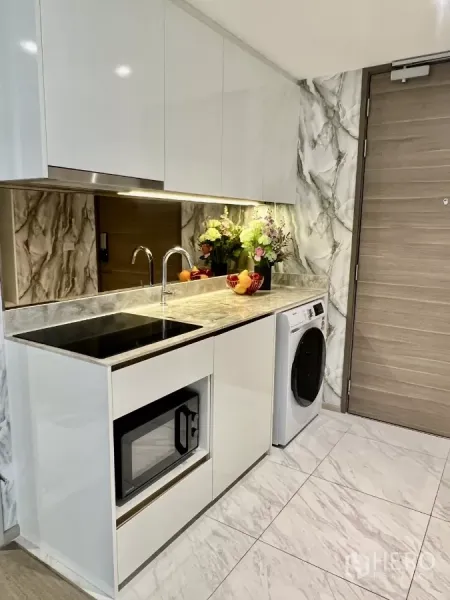 Condominium for rent in Khlong Toei, Bangkok - Sleek kitchenette with glossy cabinets, induction hob, sink, microwave and washing machine.