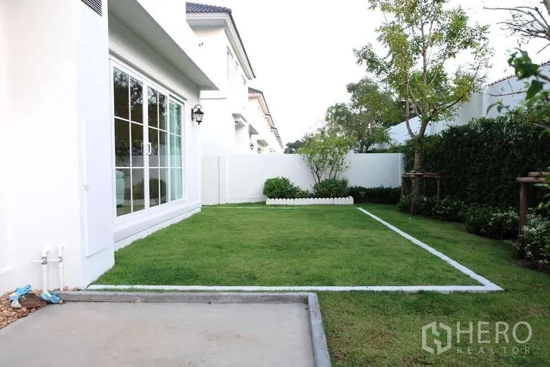 Detached House for rent in Bang Phli, Samut Prakan - Lush backyard with lawn, hedges and sliding glass doors to the living room.
