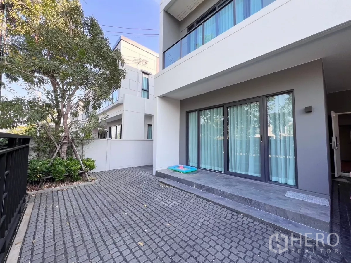 Detached House for rent in Bang Phli, Samut Prakan - Paved front patio with sliding glass doors, landscaped tree and privacy fence.