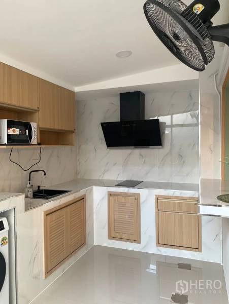 Townhouse for rent in Bang Phli, Samut Prakan - Modern kitchen with marble-look walls, black hood, induction hob and wood cabinetry.