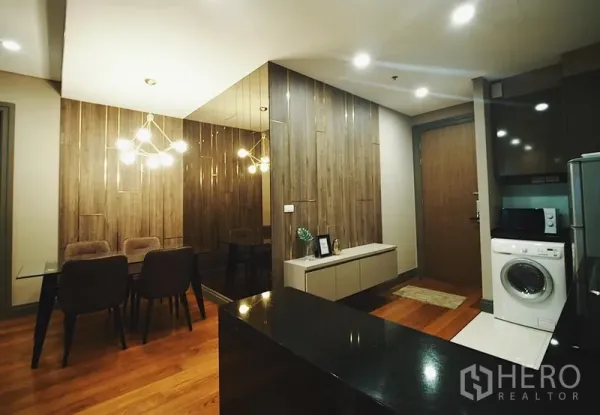 Condominium for rent in Khlong Toei, Bangkok - Dining corner with pendant lights, mirrored wall and kitchen with washing machine.