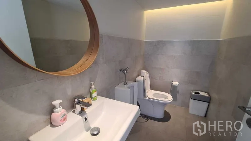 Detached House for rent in Watthana, Bangkok - Guest bathroom with large round mirror, vanity and toilet.