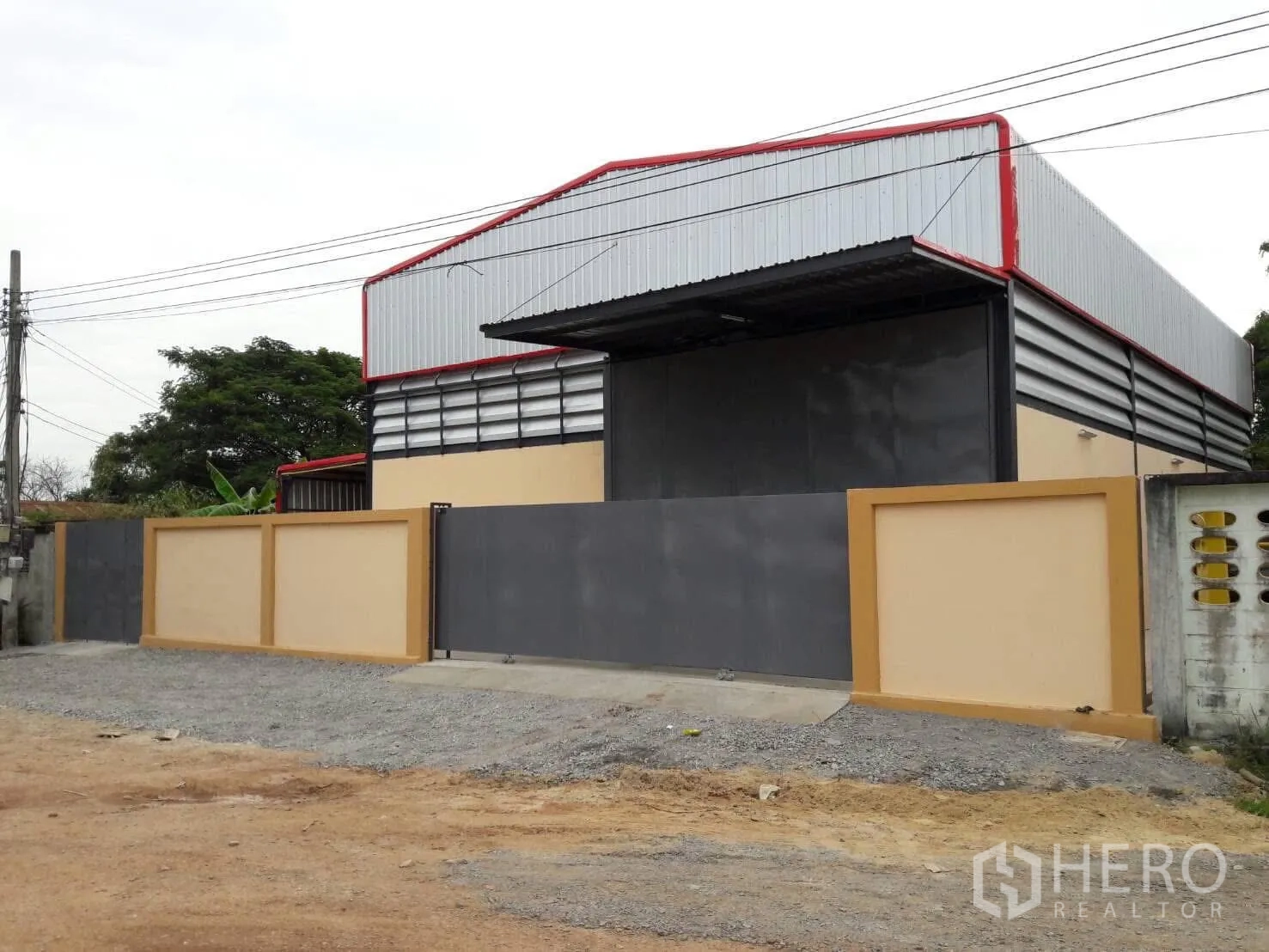 Warehouse for rent or sale in Khlong Toei, Bangkok - Gated modern steel warehouse with high gable roof and gravel driveway in Khlong Toei.