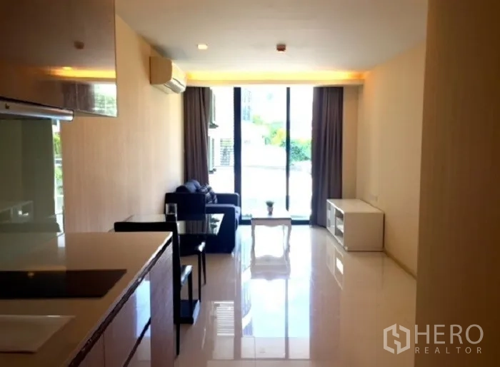 Condominium for rent or sale in Pathum Wan, Bangkok - Sunlit living room with sofa, dining table and sliding doors to the balcony next to the kitchenette.