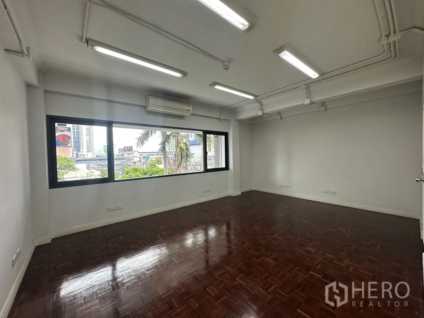 Office Space for rent in Watthana, Bangkok - Corner office area with wide window, AC unit, and urban views over greenery.