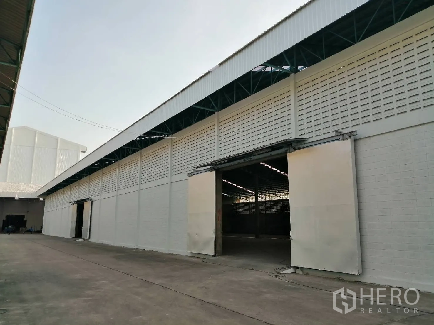 Warehouse for rent in Mueang Pathum Thani, Pathum Thani - Long warehouse facade with open sliding doors and a covered loading lane inside the compound.