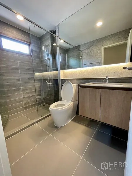 Detached House for rent in Bang Kapi, Bangkok - Modern bathroom with glass-enclosed shower, full-width mirror and gray tiles.