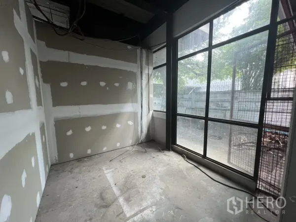 Retail Space for rent in Watthana, Bangkok - Unfinished room with drywall and floor-to-ceiling windows facing a fence and trees.