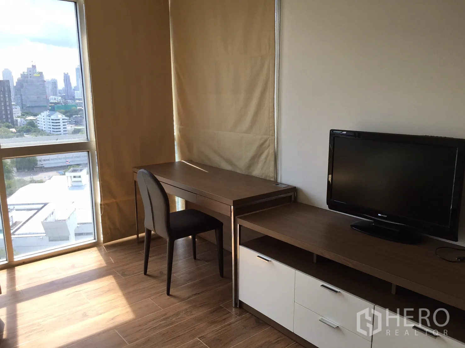 Condominium for rent or sale in Khlong Toei, Bangkok - Corner study with desk beside floor-to-ceiling windows and a TV console.
