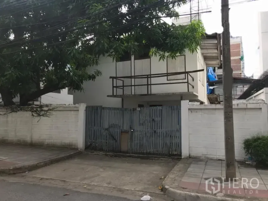 Detached House for rent in Sathon, Bangkok - Gated two-storey detached house with white boundary wall and a large shade tree on a quiet lane in Sathon, Bangkok.