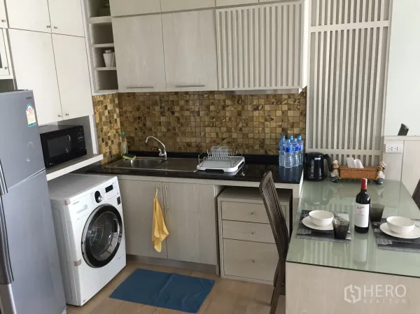 Condominium for rent in Bangkok - Modern kitchenette with mosaic backsplash, sink, microwave, fridge, washer and glass dining table.