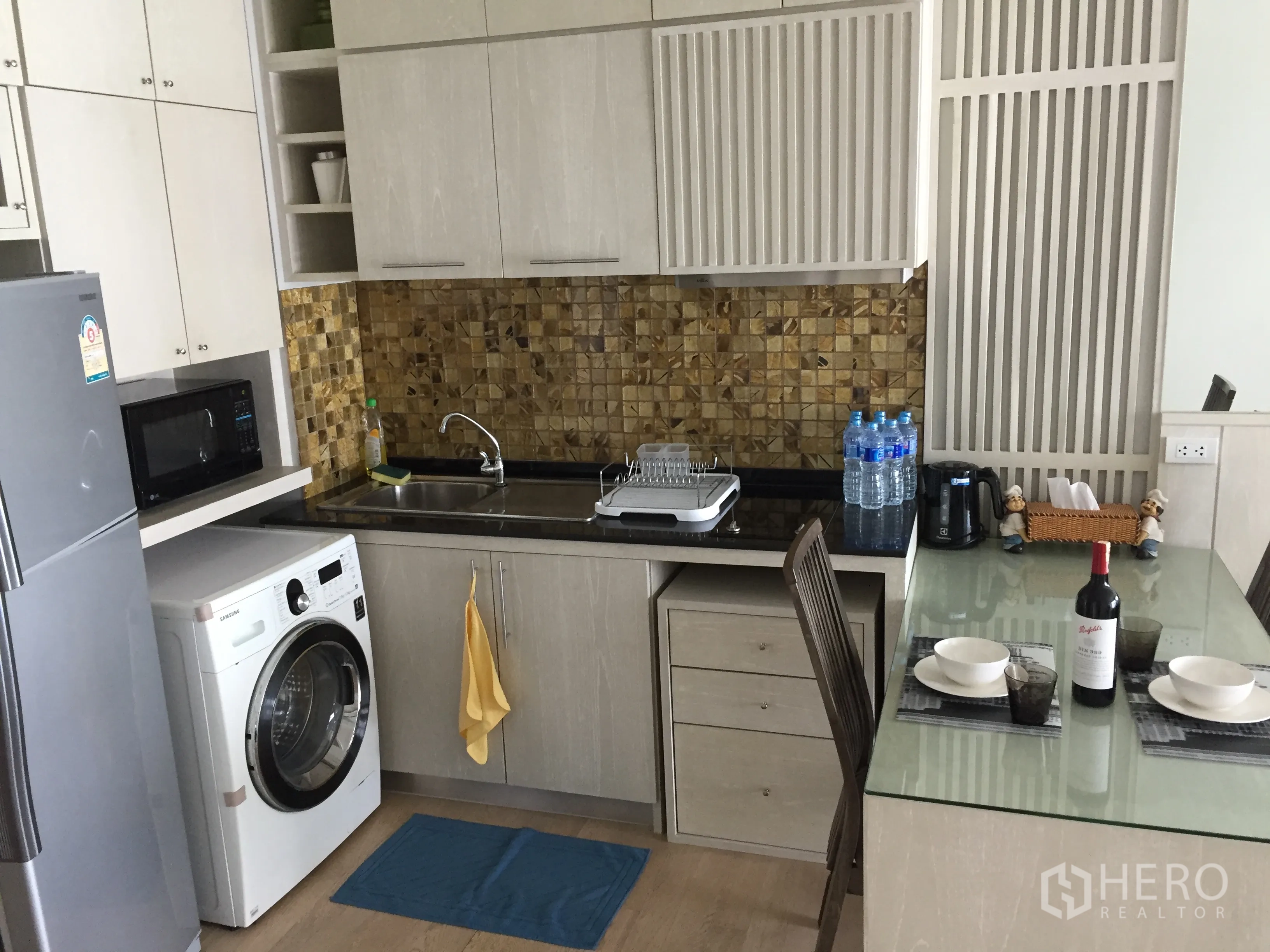 Condominium for rent in Bangkok - Modern kitchenette with mosaic backsplash, sink, microwave, fridge, washer and glass dining table.