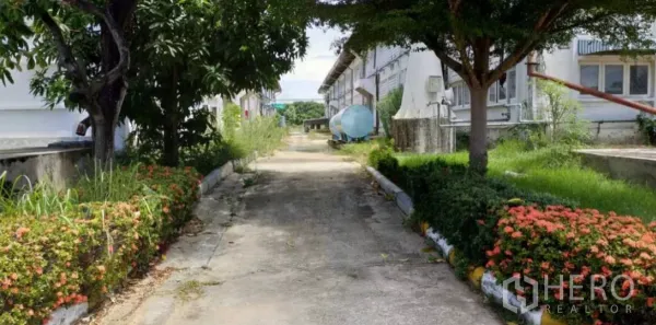 Factory for rent in Bang Pakong, Chachoengsao - Narrow landscaped service lane with shrubs, mature trees and a water tank between factory blocks.
