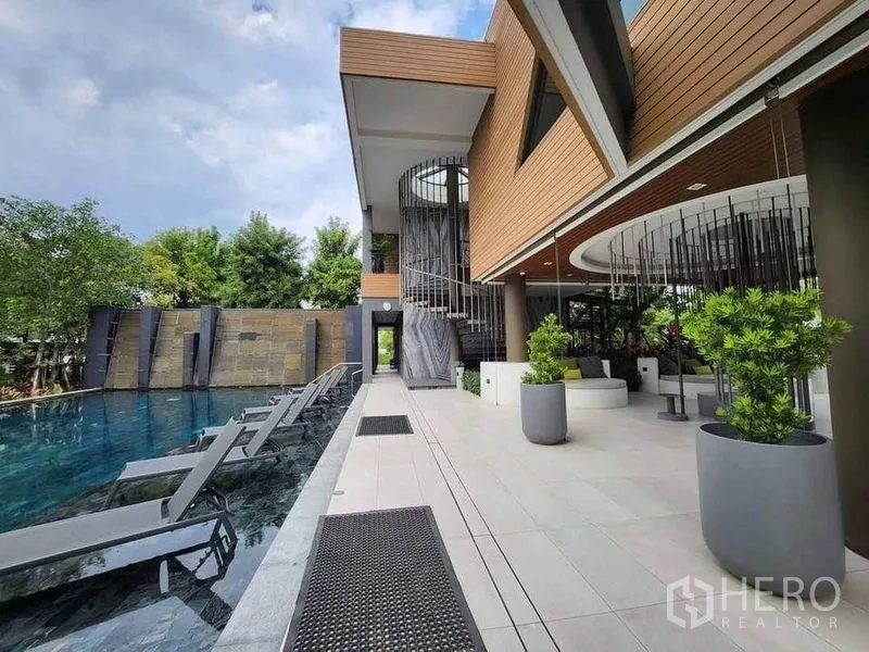 独立式住宅 出售在Sai Mai, Bangkok - 现代会所配螺旋楼梯，旁为长形游泳池与日光躺椅及绿植。
