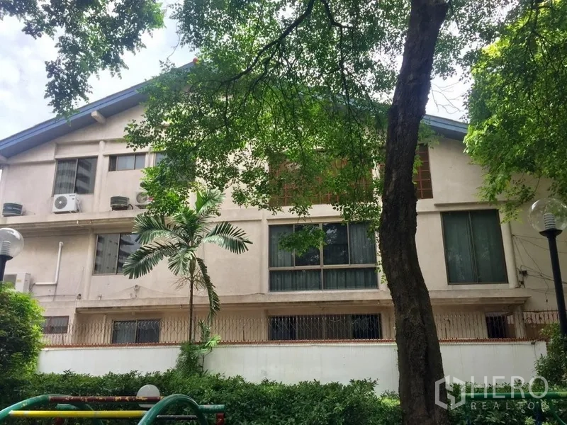 Townhouse for rent in Watthana, Bangkok - Side exterior of the townhouse shaded by mature trees beside a small playground.