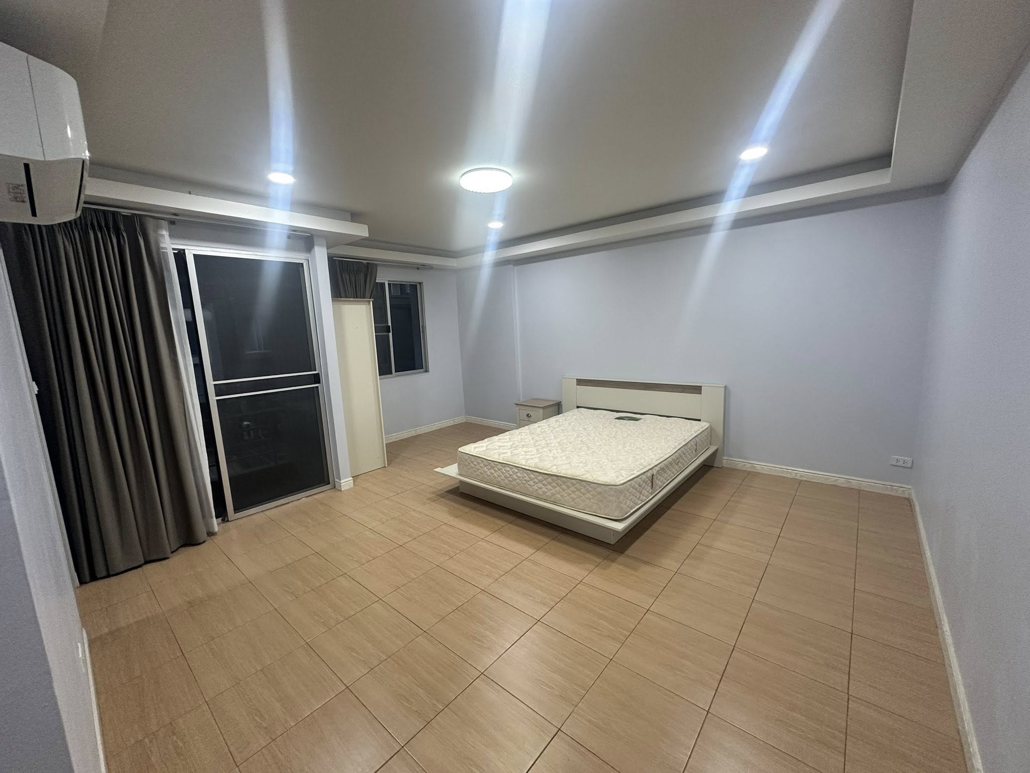 Home Office for rent in Wang Thonglang, Bangkok - Large bedroom with bed, wood-look tiles, sliding balcony door and curtains.