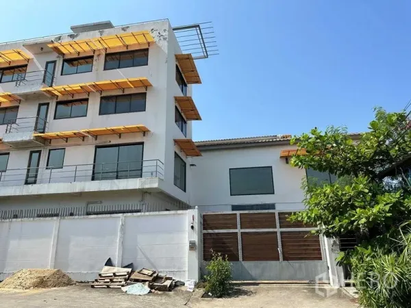 Warehouse for rent in Phra Khanong, Bangkok - Exterior of the warehouse with attached multi-storey office building, yellow sunshades and gated entrance.