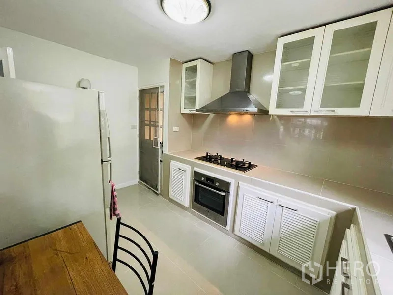 Detached House for rent in Watthana, Bangkok - Modern kitchen with gas hob, oven, range hood, and white cabinets.