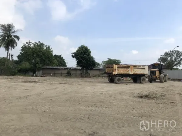 Factory for rent in Phra Nakhon Si Ayutthaya - Leveled dirt yard with a dump truck and tractor beside a perimeter wall and trees under a blue sky.