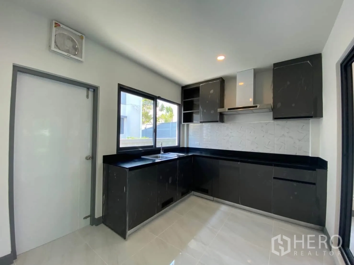 Detached House for rent or sale in Prawet, Bangkok - Modern L-shaped kitchen with black cabinets, stone countertops, window, and range hood.