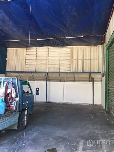 Warehouse for rent in Suan Luang, Bangkok - Covered loading area with roller shutters and a high roof canopy beside a small truck.