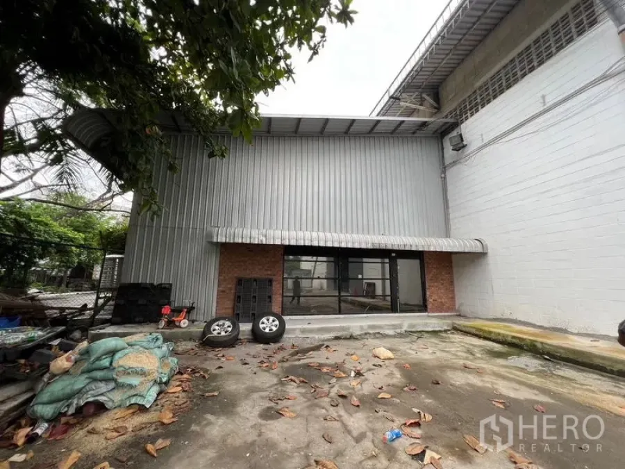 Warehouse for rent in Suan Luang, Bangkok - Suan Luang Bangkok warehouse exterior with corrugated metal cladding, brick accents, glass entry, and a small loading forecourt.