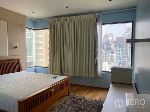 Condominium for rent - Bright bedroom with corner windows and city skyline view, wooden bed frame and rug.