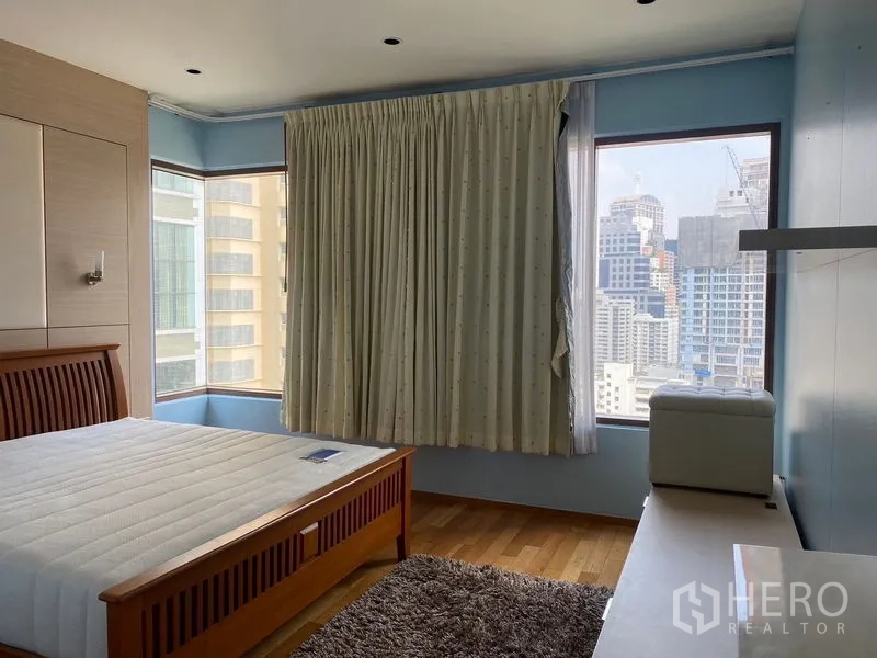 Condominium for rent - Bright bedroom with corner windows and city skyline view, wooden bed frame and rug.
