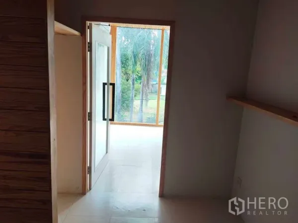 Office Space for rent in Khlong Toei, Bangkok - Interior corridor with a glass door leading to a bright meeting nook by large windows and garden views, with a floating shelf.