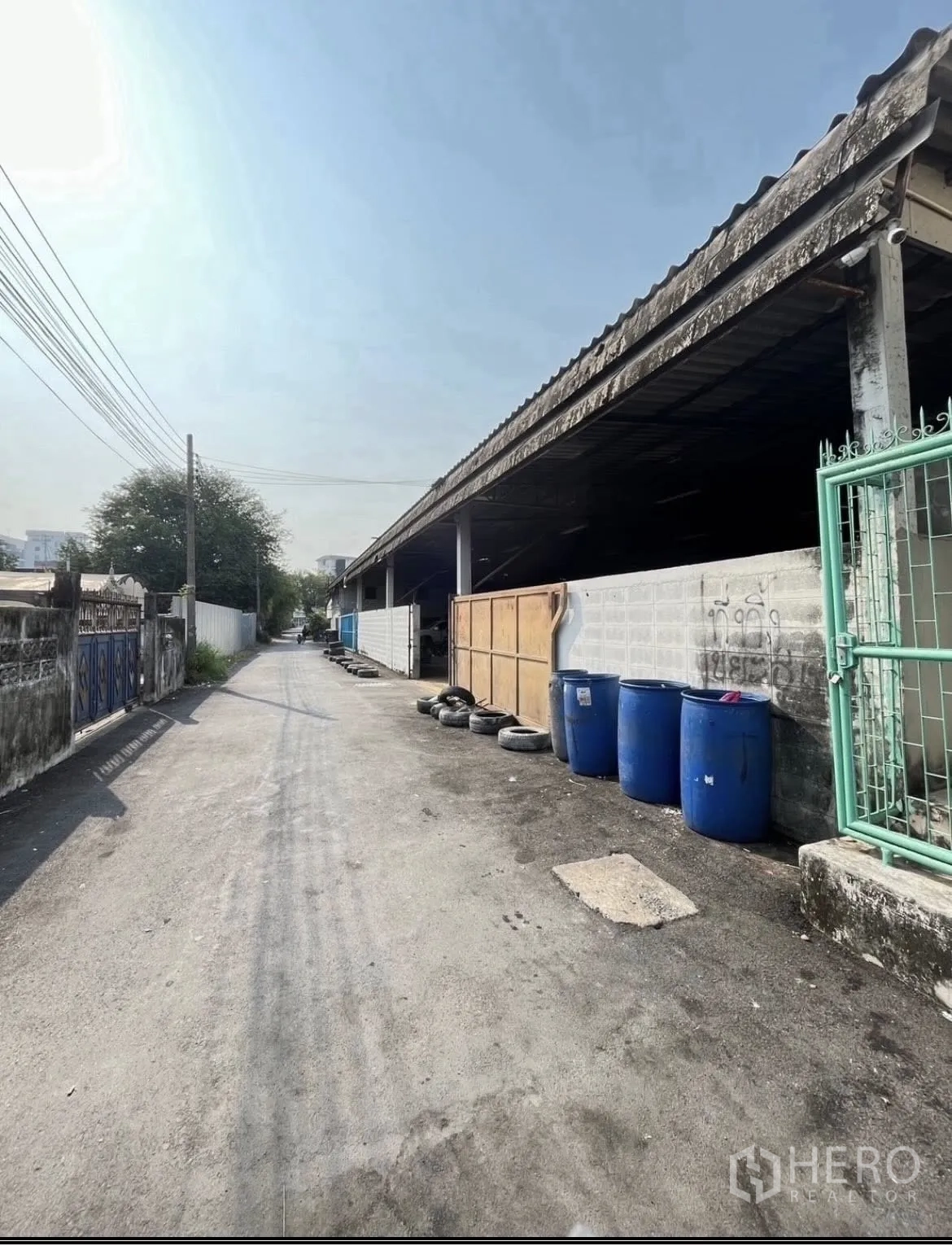 Warehouse for rent in Chatuchak, Bangkok - Exterior side of the warehouse along the lane with barrels and tires near the wall.