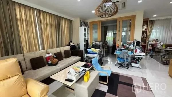 Detached House for sale in Suan Luang, Bangkok - Bright living room with large windows, L-shaped sofa, and adjoining study and dining area.