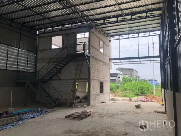 Warehouse for rent in Lam Luk Ka, Pathum Thani - Open-plan warehouse bay with two-storey office block and stairs, large entrance opening.