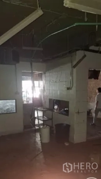 Shophouse for rent or sale in Watthana, Bangkok - Dim service area with tiled back rooms, visible piping and wiring in a raw commercial interior.