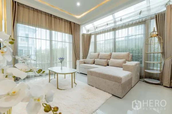 独立式住宅 出租或出售在Bang Khen, Bangkok - 采光充足的会客区，L型沙发、弧形落地窗与圆形茶几和柔软地毯。