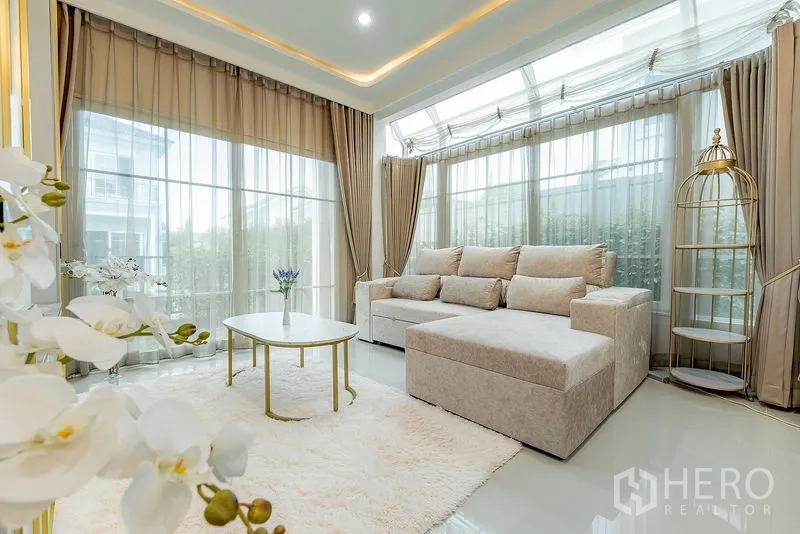 独立式住宅 出租或出售在Bang Khen, Bangkok - 采光充足的会客区，L型沙发、弧形落地窗与圆形茶几和柔软地毯。